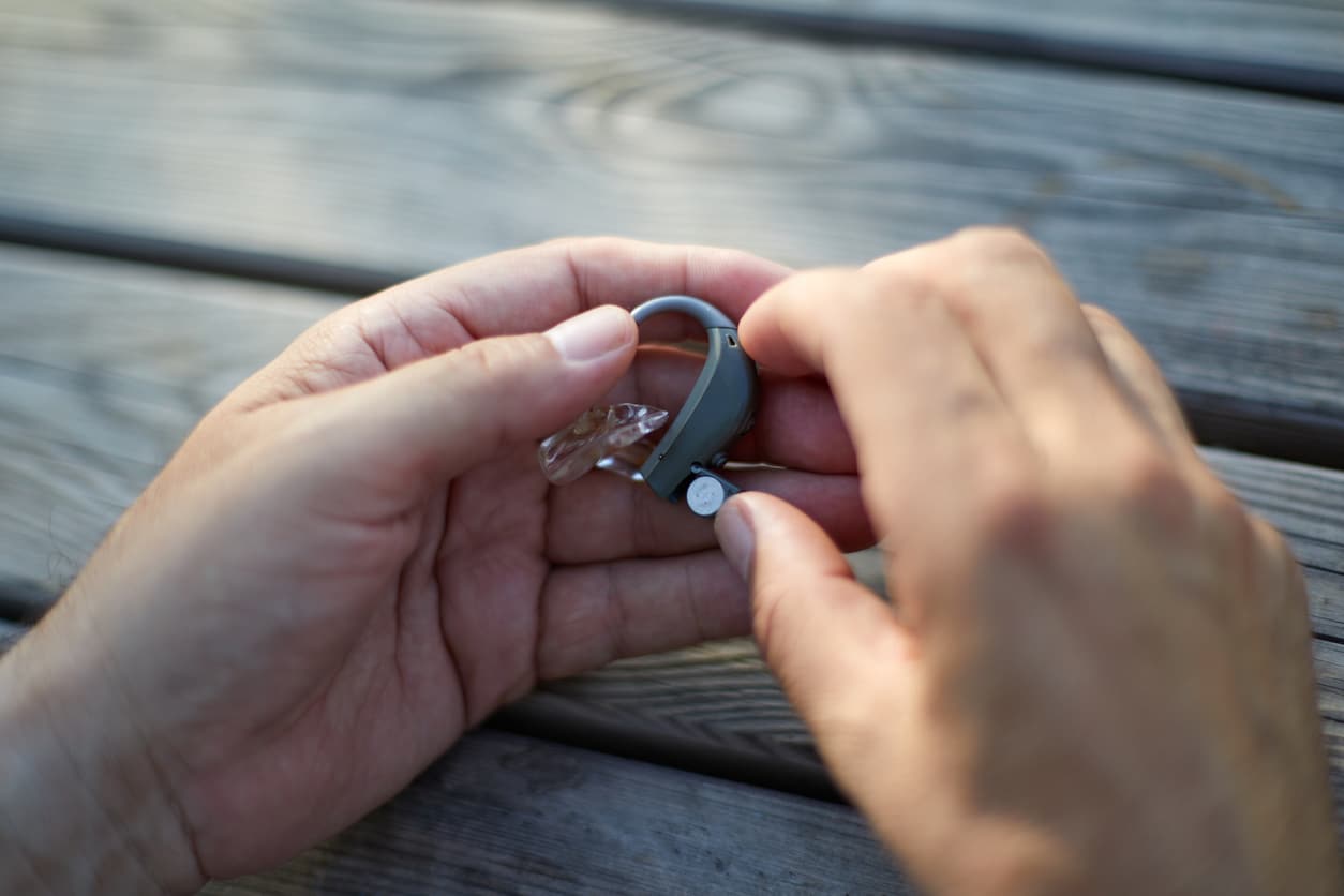 Close up of someone holding their hearing aids at a table, troubleshooting feedback issues. 